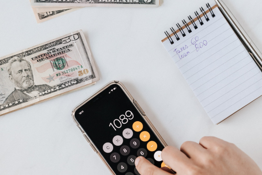 Calculator app on iPhone with money and notebook sitting on a table