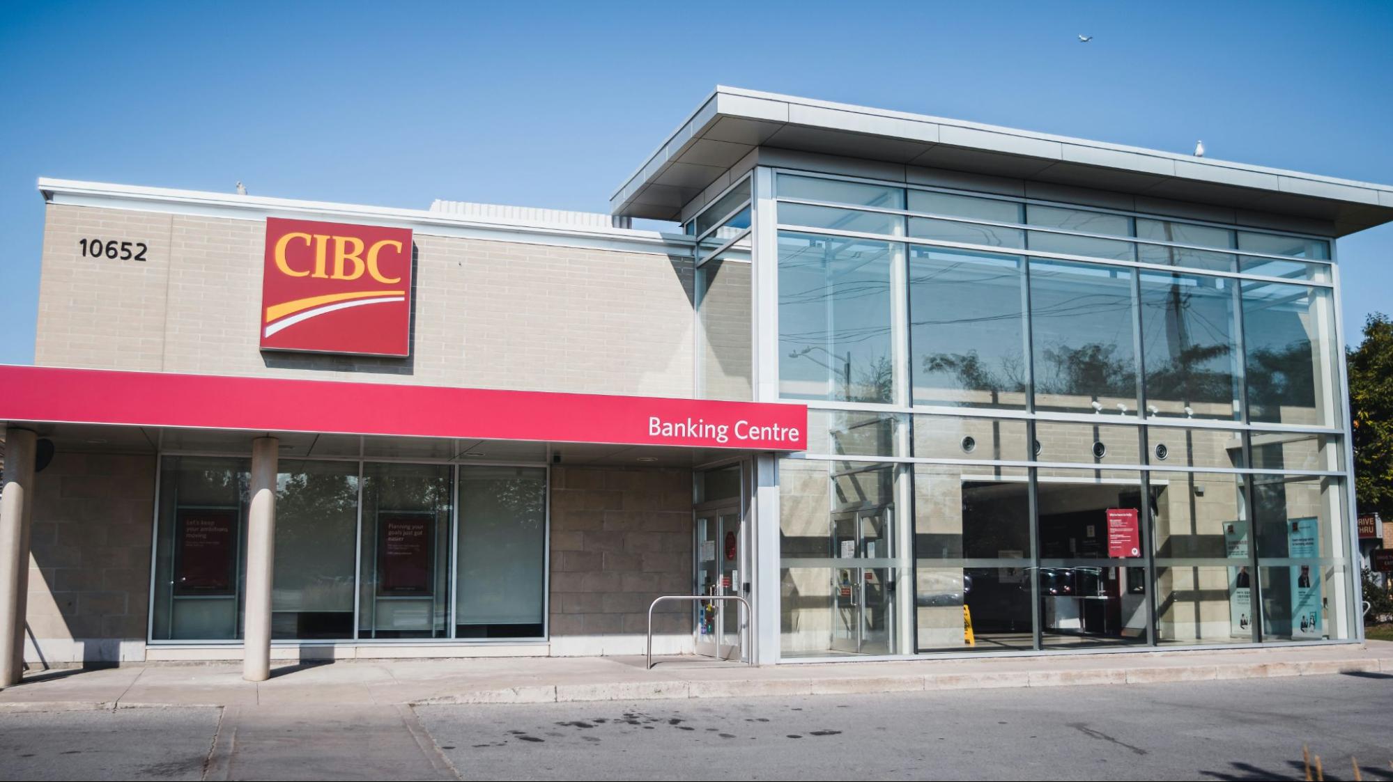 Modern CIBC Banking Centre branch with glass facade, red signage, and clear blue sky in daylight setting