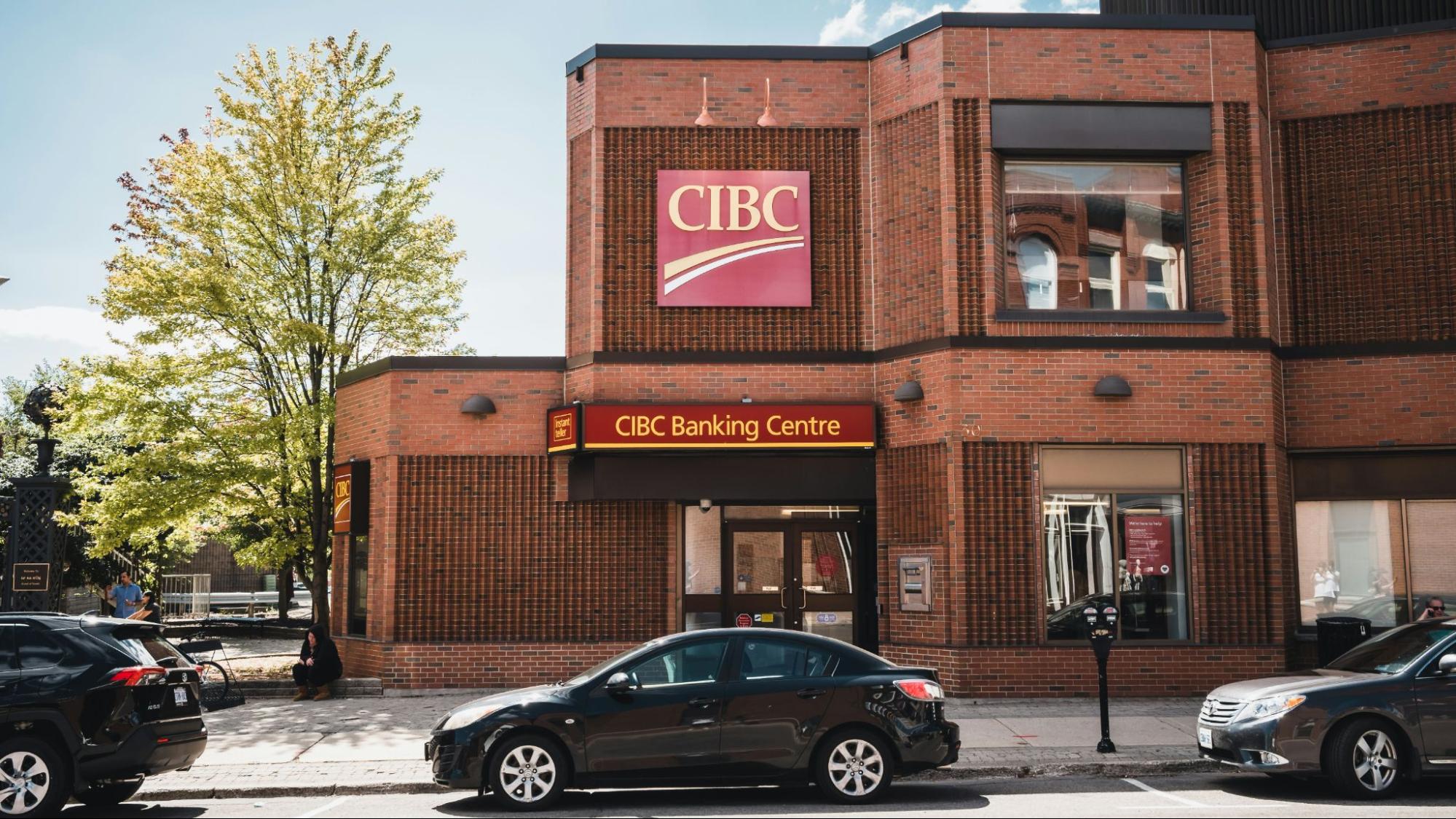 Street view of CIBC Banking Centre in a brick building with parked cars, trees, and bank signage visible