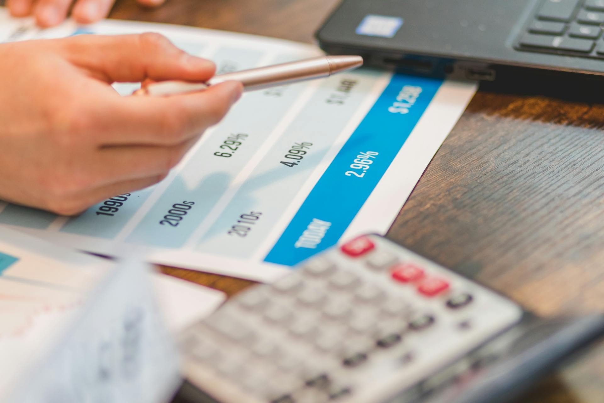 Hand holding a bank card over a calculator and laptop while checking a currency conversion