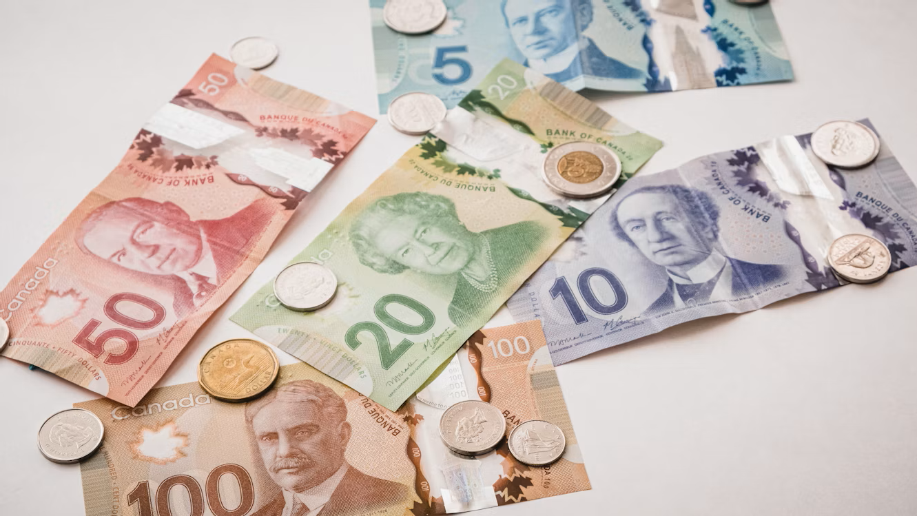 Canadian banknotes in $5 to $100 denominations with loonies, toonies, and quarters