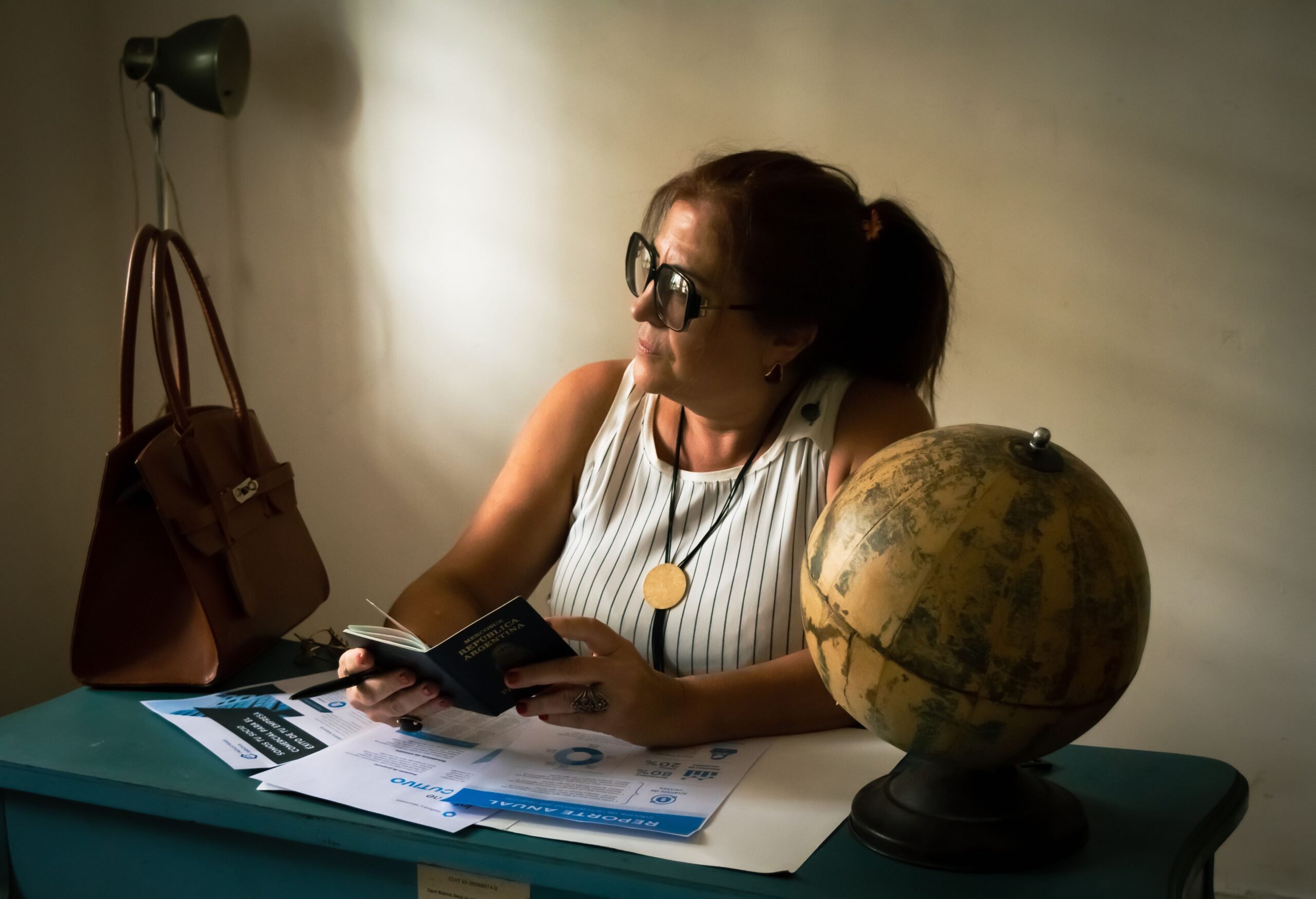Woman at a kitchen table with a passport and a globe, planning a trip abroad